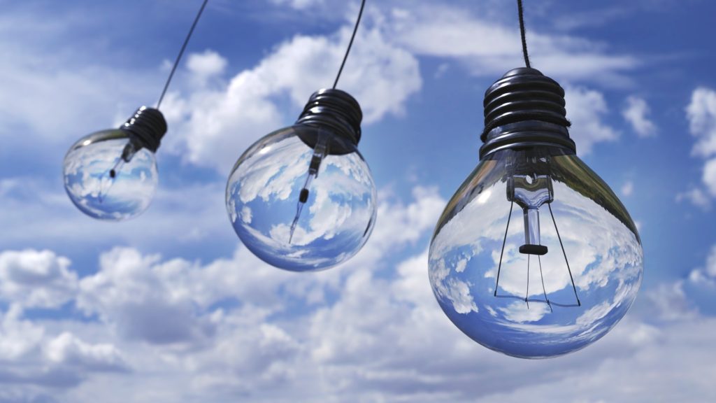 A picture of three lightbulbs seemingly hanging from the sky with blue and white clouds in the background. This abstract view is meant to prepare readers for an article about a popular cloud computing solution known as database-as-a-service or DBaaS solutions.
